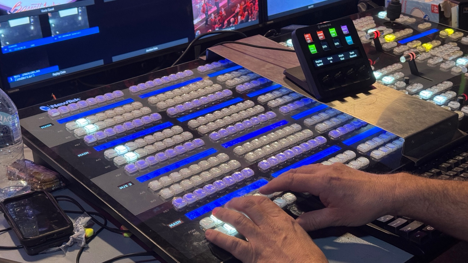 Hands operating a NewTek video switcher with Barrett-Jackson feeds on the production monitors