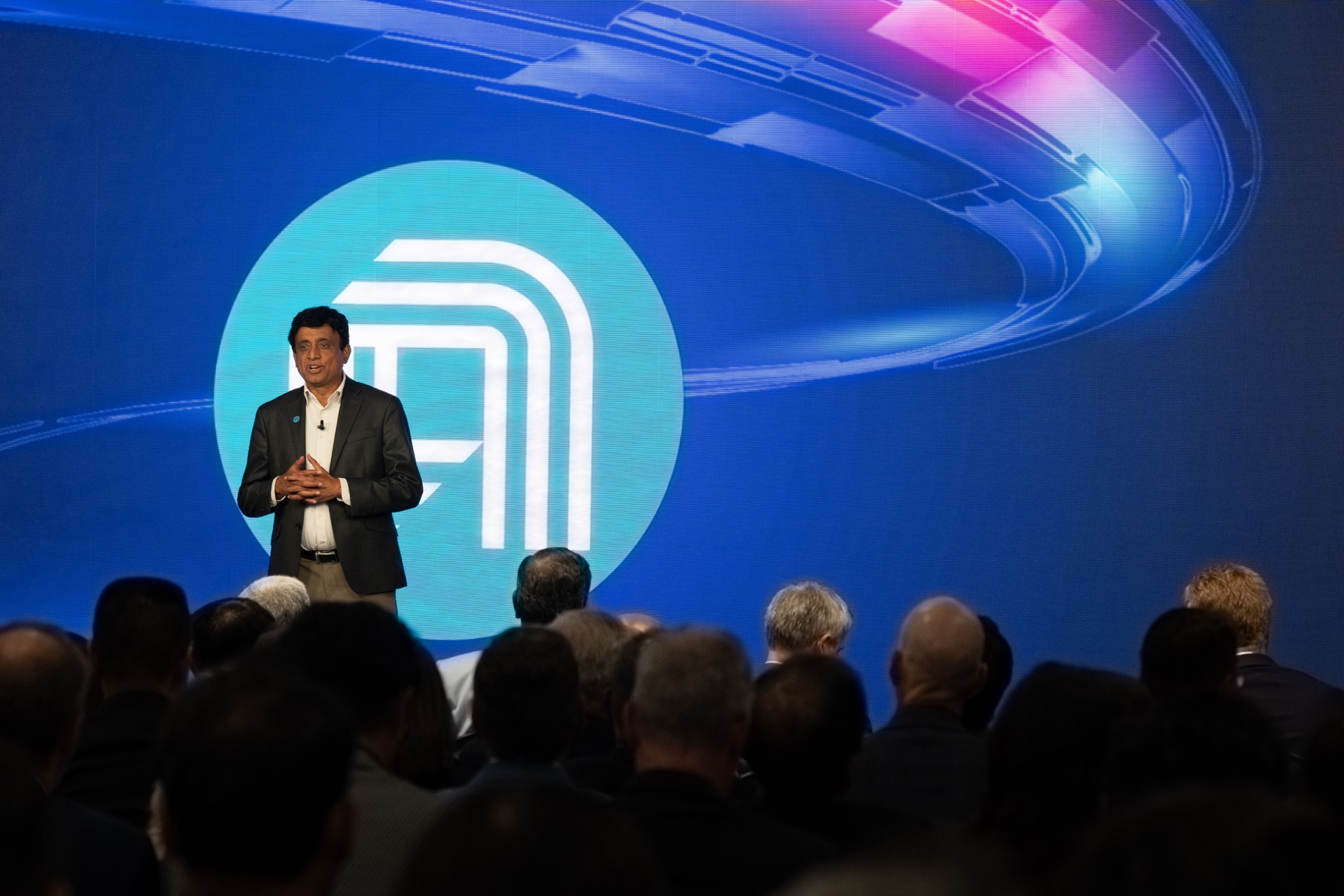 Prabu Raja presenting at the EPIC Center unveiling in front of a large blue Applied Materials LED backdrop and a seated audience
